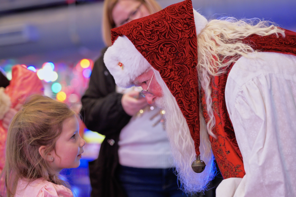 A child greets Santa Claus, who leans in for a warm, festive conversation at a colorful holiday event.