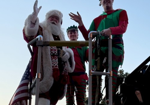 Santa and two people dressed as elves are standing on a decorated fire truck, waving.