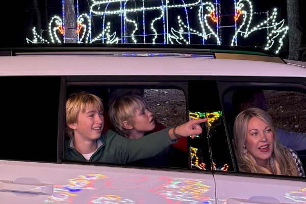 A family in a car at night enjoying festive lights and decorations above their vehicle.