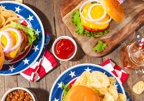 American-style burgers, potato chips, watermelon, baked beans, and soft drinks are arranged on a rustic wooden table for a casual meal.