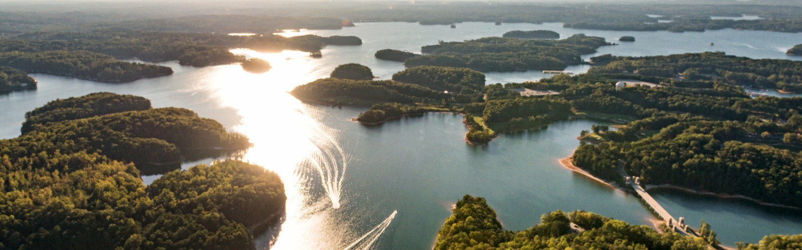 Bird's-eye view of a large, scenic lake dotted with numerous islands, surrounded by lush green forests and sunny skies.