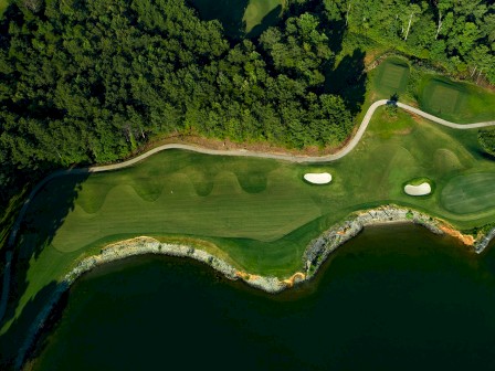 Aerial view of a golf course with a green fairway, two sand bunkers, and a water body adjacent to the course.