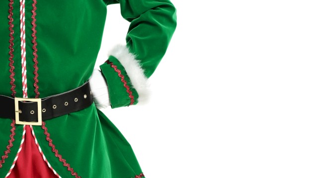 The image shows a person dressed in a green Christmas elf costume with red and white accents, red pants, and a black belt with a gold buckle.