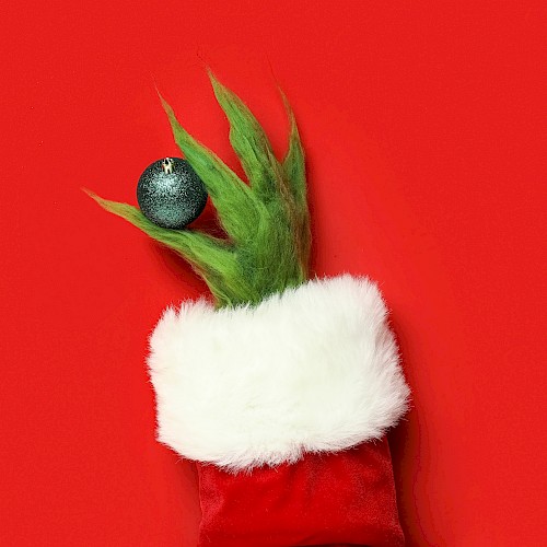A festive puppet resembling a Christmas tree with a green spiky top, white fur cuff, and a blue ornament on a red background.