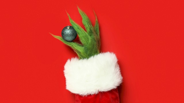 A festive puppet resembling a Christmas tree with a green spiky top, white fur cuff, and a blue ornament on a red background.