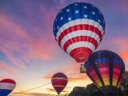 Colorful hot air balloons fly at sunrise, creating a vibrant sky filled with shades of pink, purple, and orange.