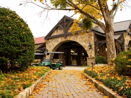 A stone building with colorful fall leaves, trees, and a golf cart at the entrance on a chilly autumn day.