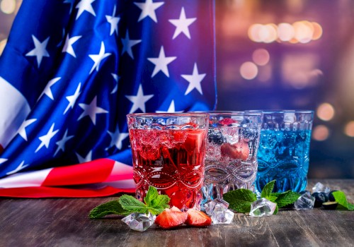 Colorful patriotic drinks with ice, strawberries, and mint leaves are in front of an American flag for a celebration.