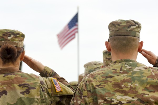 Soldiers in camouflage salute an American flag during a ceremony.