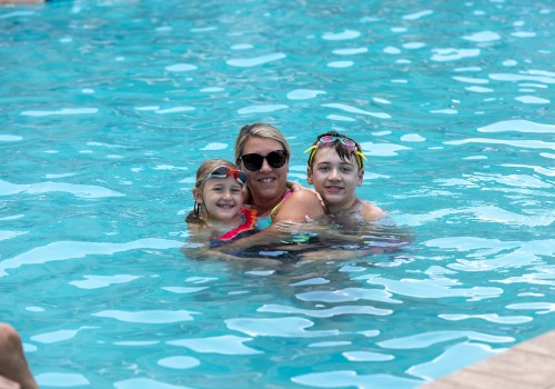 A woman with two children enjoy swimming and smiling in a bright blue pool on a sunny day.