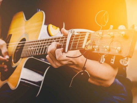 A person is playing an acoustic guitar, with sunlight softly illuminating the scene, creating a warm and serene atmosphere.