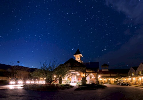 A beautifully lit building under a starry night sky with trees and parked golf carts in a peaceful, illuminated setting.