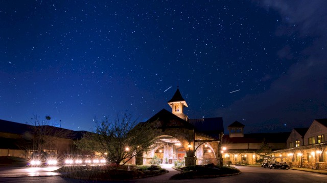 A beautifully lit building under a starry night sky with trees and parked golf carts in a peaceful, illuminated setting.