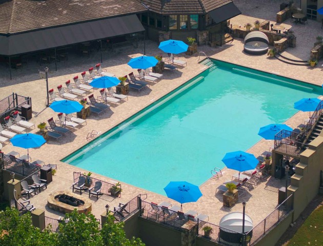 An aerial view of a hotel pool area with blue umbrellas, lounge chairs, and surrounding seating spaces.