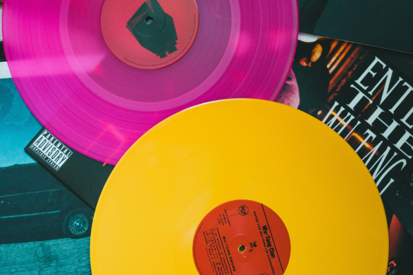Vinyl records, one pink and one yellow, are placed on album covers with bold designs and text.