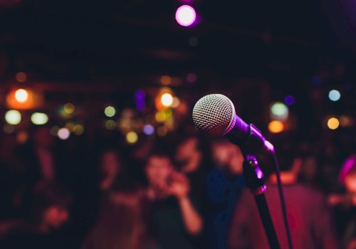 A microphone is in focus against a blurred backdrop of a crowd and colorful lights, suggesting a lively performance or event.
