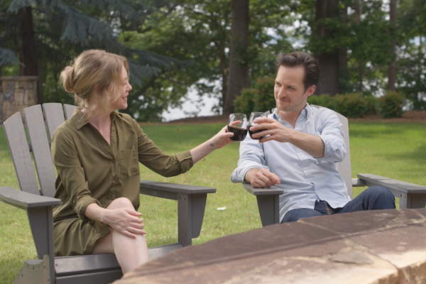 A couple seated on outdoor chairs clinking glasses in a garden setting with trees in the background.