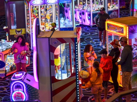 People at an arcade with colorful games and claw machines, enjoying a lively atmosphere.