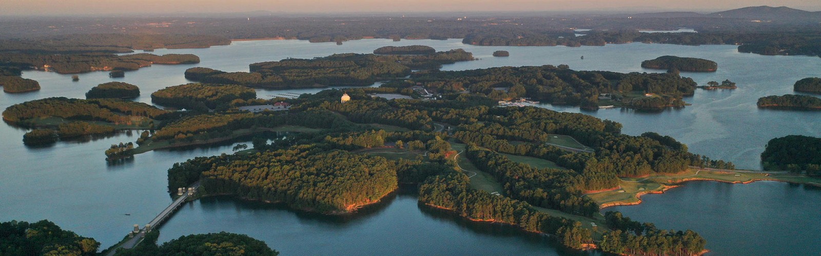 Aerial view of a lake with numerous small, forested islands at sunset. The water is calm and the surrounding landscape is lush and green.
