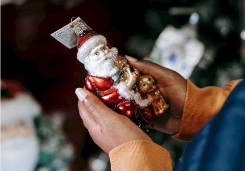 A person holding a Santa Claus ornament with teddy bears, ready for Christmas decorating.