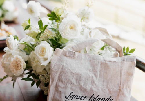 A bouquet of white roses and greenery in a beige tote bag that reads “Lanier Islands Weddings,” resting on a wooden railing.