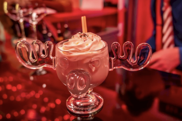 A glass shaped like a moose's head filled with a creamy drink and topped with whipped cream and sprinkles, placed on a bar counter.