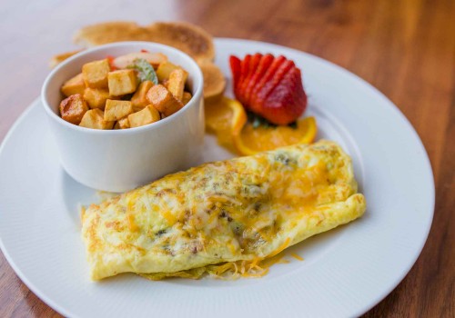 The image shows an omelet on a plate, served with a bowl of diced potatoes, sliced strawberries, orange slices, and pancakes.