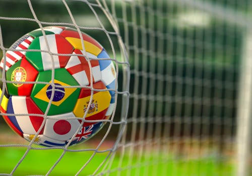 A soccer ball with national flags, including Portugal, Brazil, Japan, and the UK, caught in a goal net on a field.