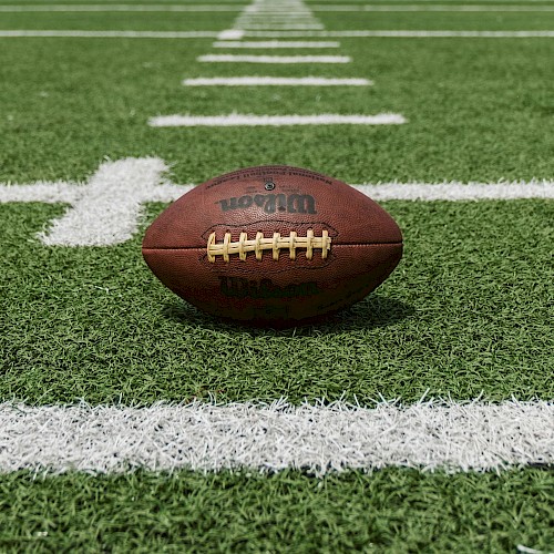 A football rests on a green field with white yard lines marking the surface.