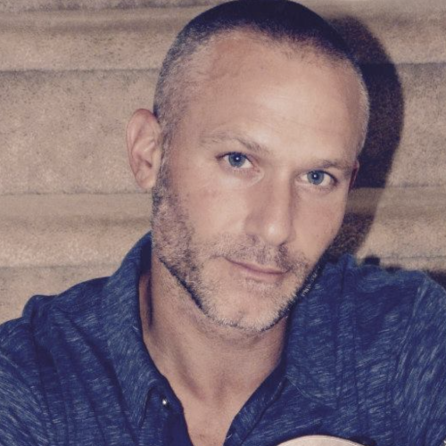 A person with a tattoo is holding an acoustic guitar while sitting.