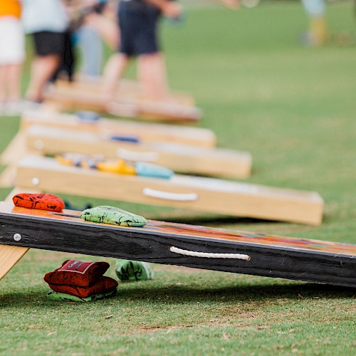 People playing cornhole on a grassy field, boards set up with bean bags ready to toss in the distance.