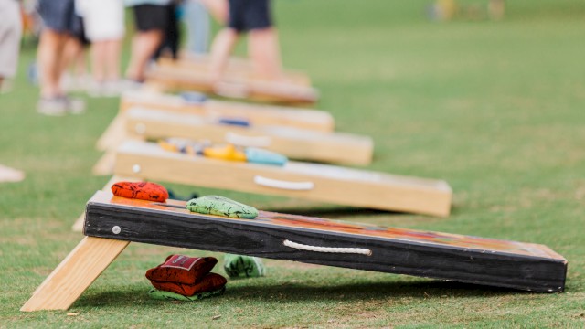 People playing cornhole on a grassy field, boards set up with bean bags ready to toss in the distance.
