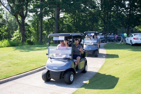 People are driving golf carts on a sunny day, surrounded by lush greenery.