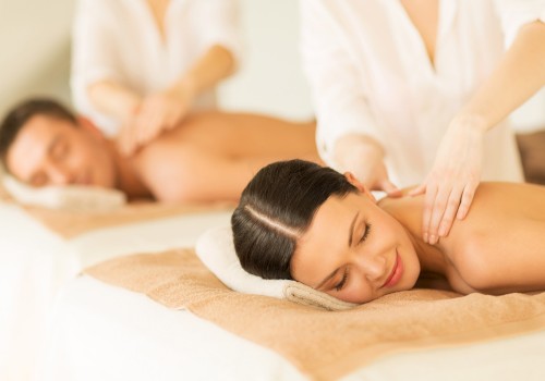 Two people are receiving a relaxing massage while lying on spa beds, with therapists attending to them in a calm environment.
