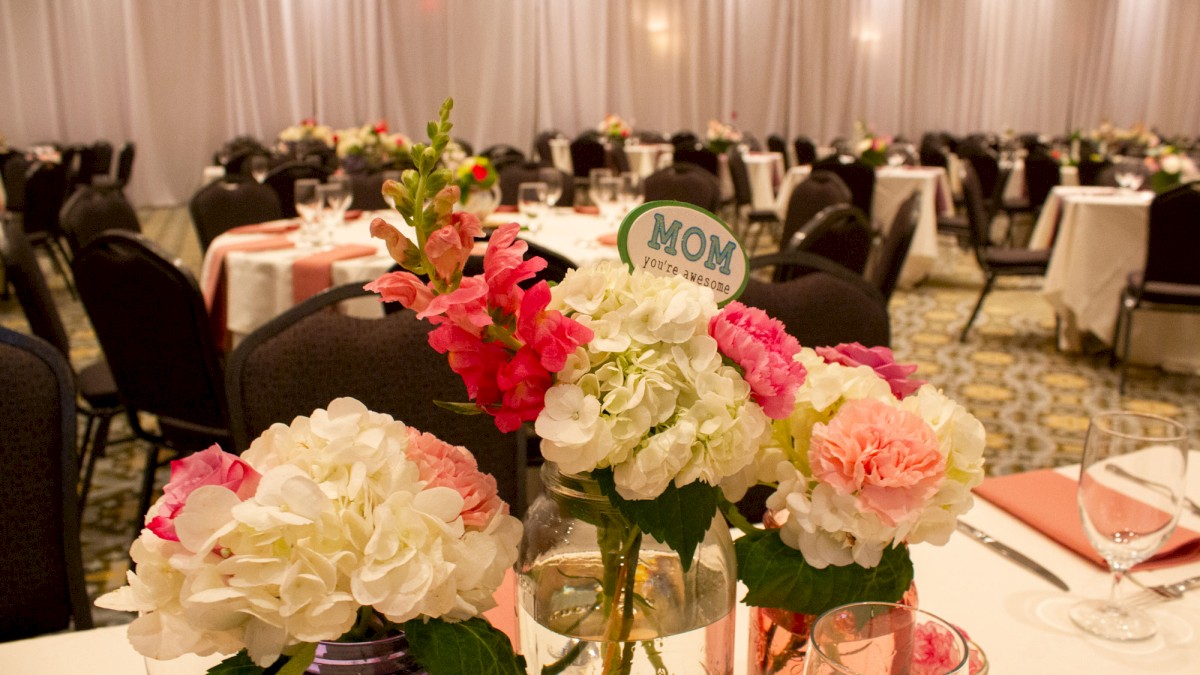 A decorated event space with floral centerpieces in jars, featuring a sign that reads 