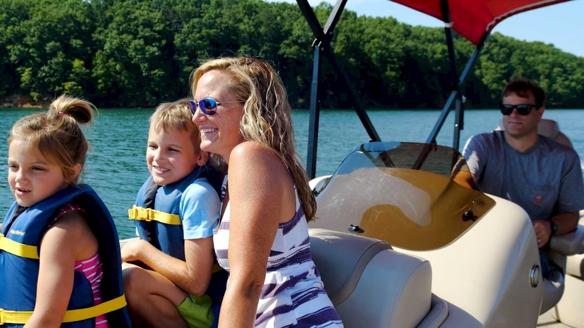 A group of people enjoy a boat ride on a lake, with two children in life jackets, a woman smiling, and a man steering the boat.