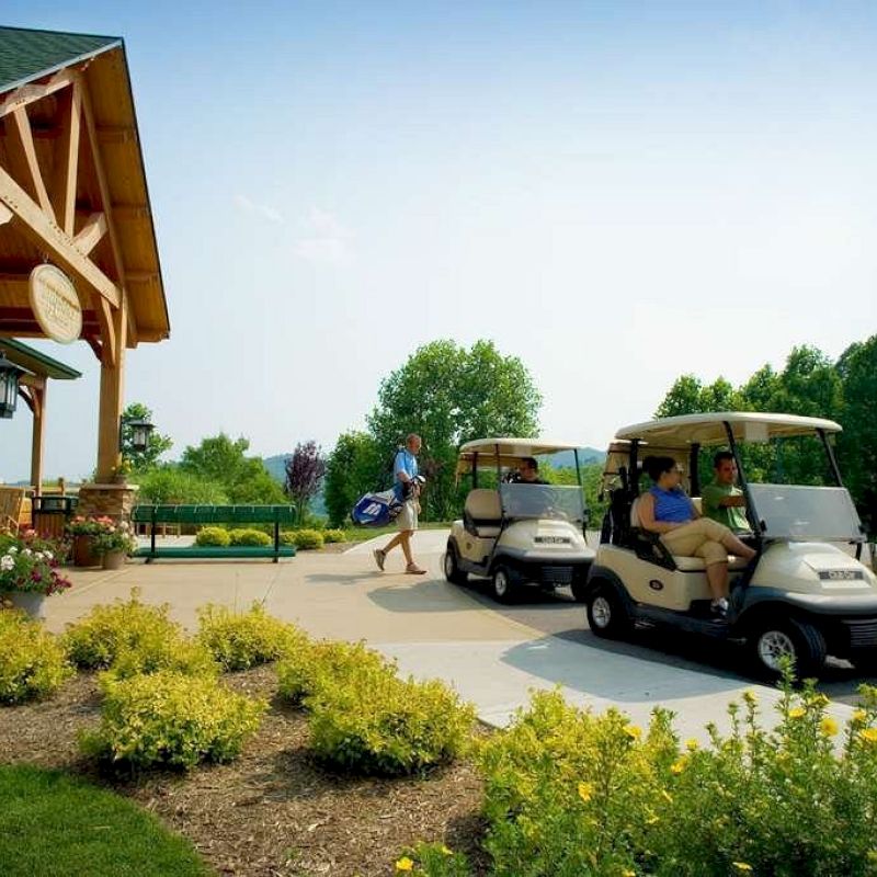 People are getting ready to use golf carts near a building with a green roof. There are plants and well-manicured bushes in the foreground.