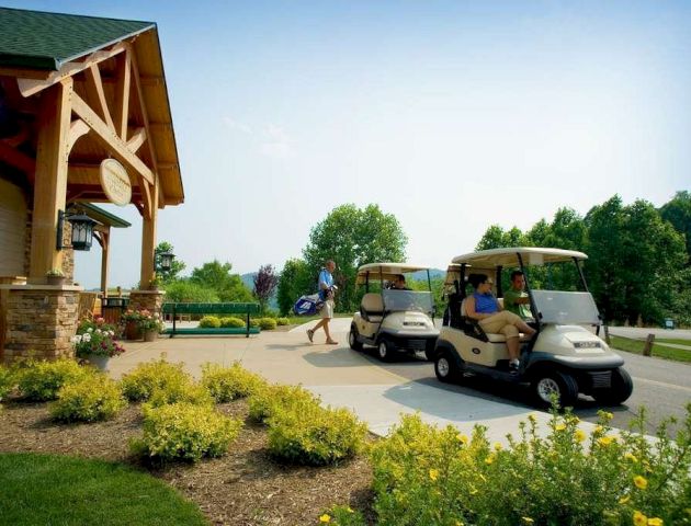 Golf carts parked outside a building with a rustic design. A person is walking away carrying a golf bag. Yellow flowers decorate the foreground.